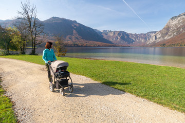 Young woman walks by the lake with a stroller. Woman with baby trolley in by Bohinj lake, Slovenia....
