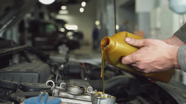 Car mechanic pouring oil into engine.