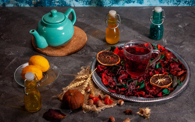 Red Hot Hibiscus tea in a glass mug on a wooden table among rose petals and dry tea custard with carcade