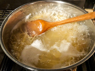 Large pan of spaghetti boiling on a cooker.