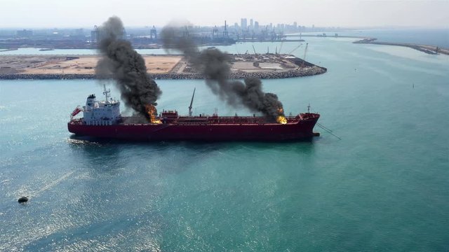 Aerial image over Oil Tanker Ship Burning Under attack Close to Harbor Aerial view with visual effect elements simulates realistic vision of Oil Tanker ship on fire with smoke .
