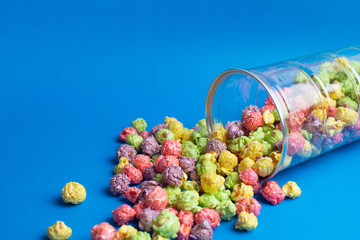 Multicolored fruit flavored popcorn in glass cups on blue background. Candy coated popcorn.