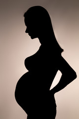 silhouette of a pregnant woman with her hair holding one hand on her lower back