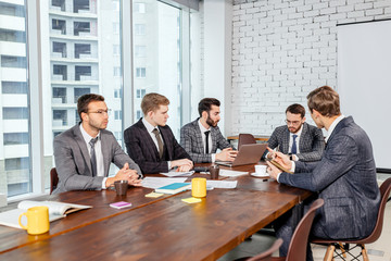 business coworking in office, young caucasian boss in stylish elegant tuxedo sit with colleagues or co-workers in modern executive office, discuss business strategies