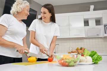 Senior woman cooking salad with granddaughter.