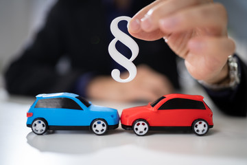 Lawyer Holding Two Small Cars And Paragraph Sign