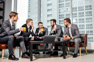 young caucasian business people talking over a cup of tea, speak about business strategies, projects and plans sitting on sofa together in office