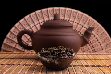 green tea in clay pot and a kettle on wooden background with a fan. food photography