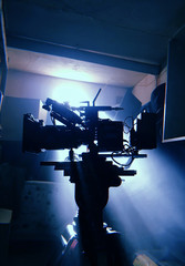 Mystical silhouette of a movie camera in the sun's rays of light from the window. Camera on a tripod in standby mode