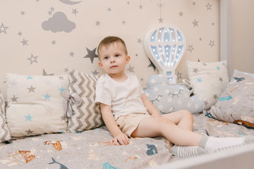 Little cute baby boy sitting in the children room in a wooden bed house with night lights in the shape of a balloon