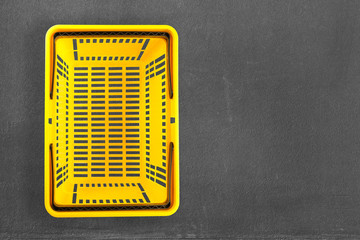 Empty yellow plastic shopping basket on black chalkboard background. Top view. Flat lay
