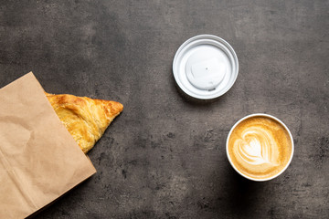 Samsa in paper envelope and cappuccino in paper cup on gray background top view