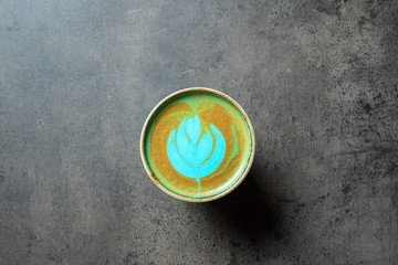 Close up of turquoise colored capuccino with latte art on gray background