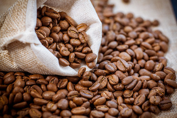 Cafe beans get enough sleep from their bag on a sackcloth background. Black coffee beans close-up. Roasted coffee beans background.