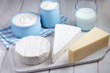 Dairy - three types of cheese, milk, and yogurt on white wooden background