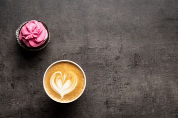 Pink cupcake and cappuccino in paper cup on gray background top view