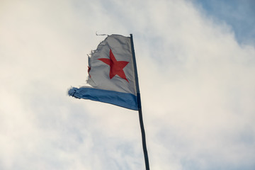 The dilapidated damaged flag of the navy of the Soviet Union is developing in the wind against the background of the sky with clouds. Part of the fabric is torn. There is a high flagpole. Background.