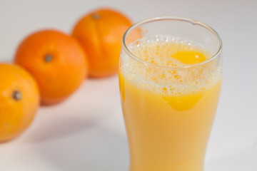Glass of orange juice on a table with oranges on the background.