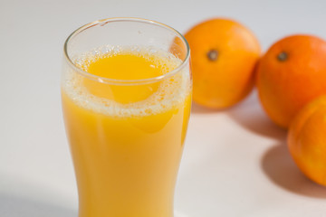 Glass of orange juice on a table with oranges on the background.