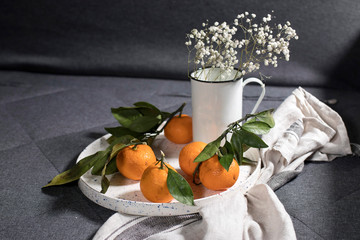 Tangerines with green leaves on white ceramic dish with a gray kitchen towel