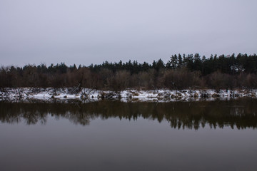 Winter landscape with river and reflections and snow on the Bank on a cloudy day