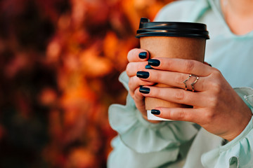 Beautiful girl in autumn street holds a cup with a hot drink in her hands