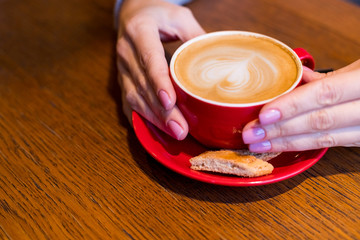 Female hands holding cup of coffee on rustic wooden table in coffee cafe. Concept relaxing in the morning. Smooth latte coffee. Toned image. selective focus.morning hot drinks.