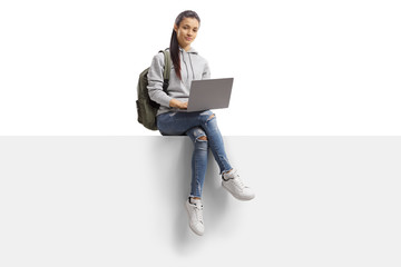Fototapeta Female student sitting on a blank panel with a laptop obraz