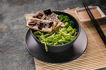 Pan-Asian cuisine. Tofu with teriyaki sauce, vegetables in a bowl, nutty spicy sauce. Vegan menu.