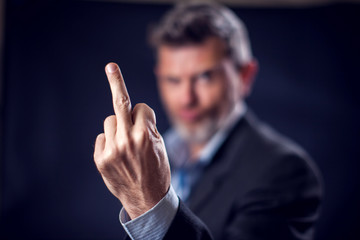 Businessman in suit showing bad gesture with finger in front of black background