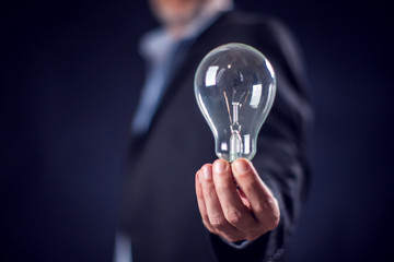 Businessman in suit holding bulb in hand in front of black background