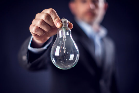 Businessman in suit holding bulb in hand in front of black background
