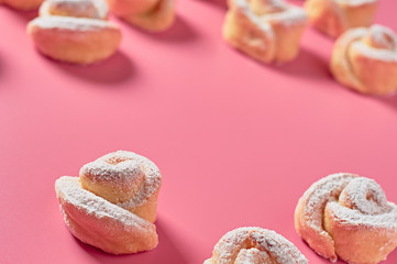 Scattered many homemade baked buns in form of rose spangled of powdered sugar lies on pink background. Space for text
