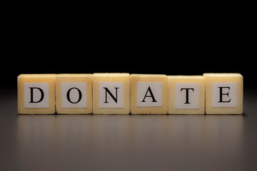 Fototapeta na wymiar The word DONATE written on wooden cubes isolated on a black background...