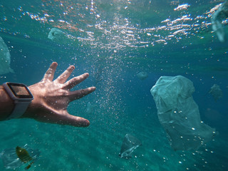 Fototapeta na wymiar A man swimming among toxic plastic wastes floating in the ocean