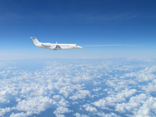 Fototapeta na wymiar White private jet business jet flies against backdrop of beautiful white clouds on blue sky