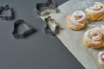 Many homemade baked buns in form of rose spangled of powdered sugar on paper near metal stencils...