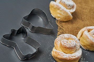 Three homemade baked buns in form of rose spangled of powdered sugar near sackcloth and metal...