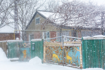Old rural house. Old metal gate with a deer pattern. Winter landscape