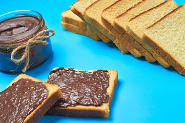 Single glass transparent jar with rope full of melted chocolate or cream near pieces of vanilla bread lies on blue desk on kitchen. Concept of nutritious breakfast or lunch