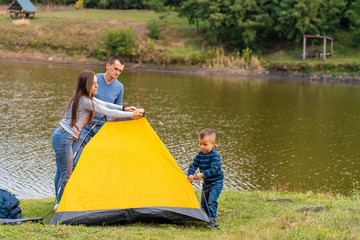 Happy family with little son set up camping tent. Happy childhood, camping trip with parents. A child helps to set up a tent