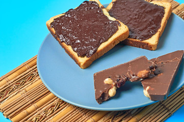 Two pieces of vanilla bread with melted chocolate on plate and bamboo mat lies on blue desk on kitchen. Concept of nutritious breakfast or lunch