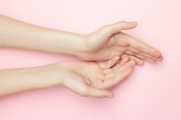 The woman hands on a pink background. Cosmetics for a sensitive skin care. Natural petal cosmetics, anti-wrinkle hand care. A thin wrist and natural manicure.