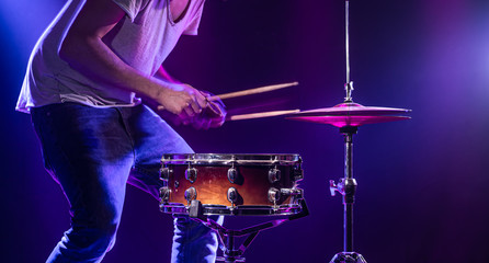 A drummer plays drums on a blue background. Beautiful special effects of light and smoke. The process of playing a musical instrument.