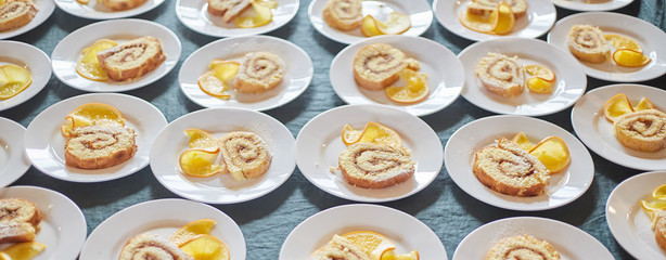 sponge rolls with jam and a slice of orange on white plates. background