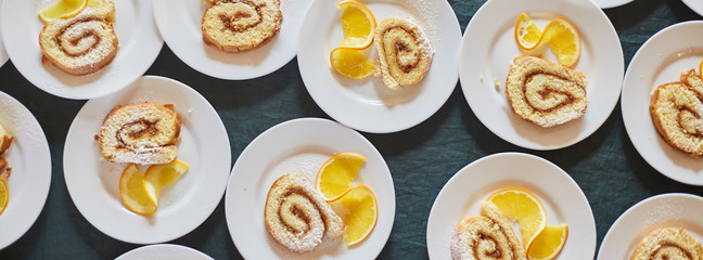 sponge rolls with jam and a slice of orange on white plates. background