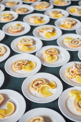 sponge rolls with jam and a slice of orange on white plates. background