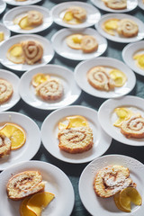 sponge rolls with jam and a slice of orange on white plates. background