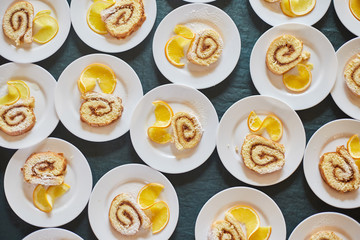 sponge rolls with jam and a slice of orange on white plates. background