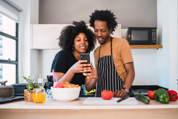Afro couple cooking together and using phone at home.